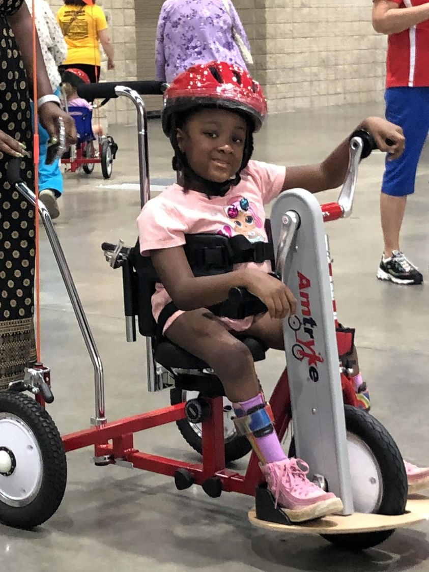 girl child riding AM16 tryke with back and foot support. And chest straps.